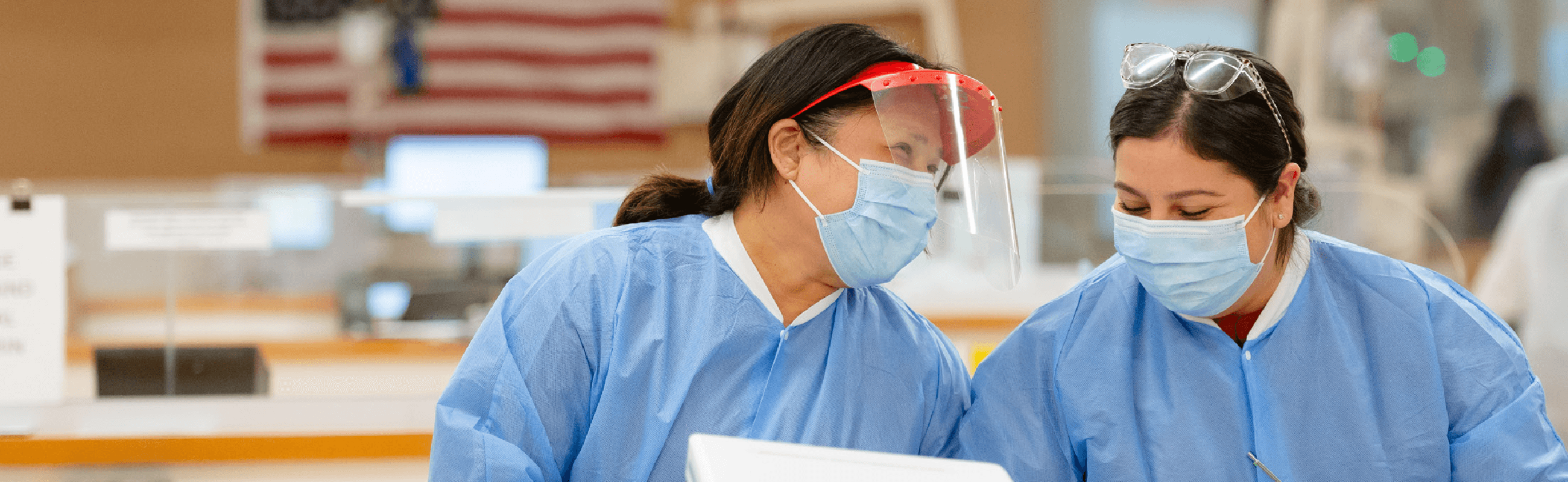 Healthcare workers in blue scrubs, surgical masks, and face shields working together in a medical setting